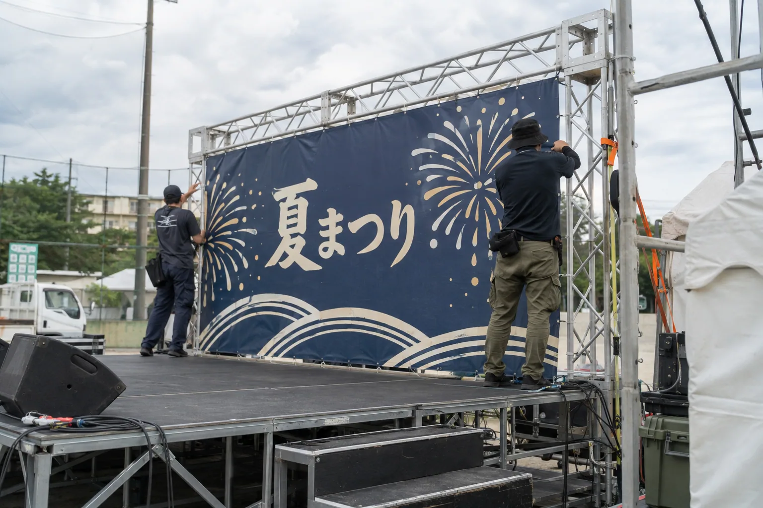 祭りのステージ背景を取り付けるスタッフの後ろ姿の生成イメージ